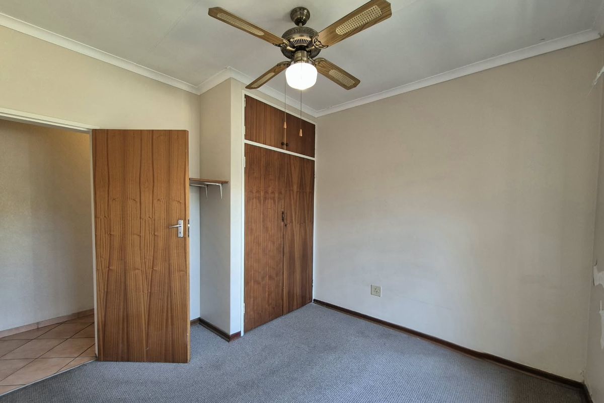 A vacant bedroom featuring built-in wooden cupboards, a ceiling fan, and carpeted flooring, offering a neutral space ready for personalization.