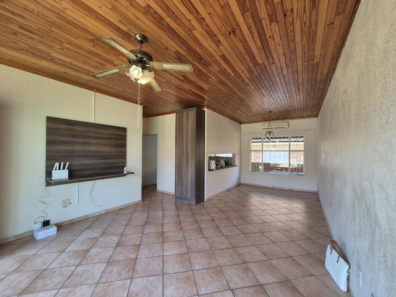 Spacious open-plan living area featuring tiled floors, a timber-clad ceiling, ceiling fan, and built-in storage, offering a versatile layout for modern living.