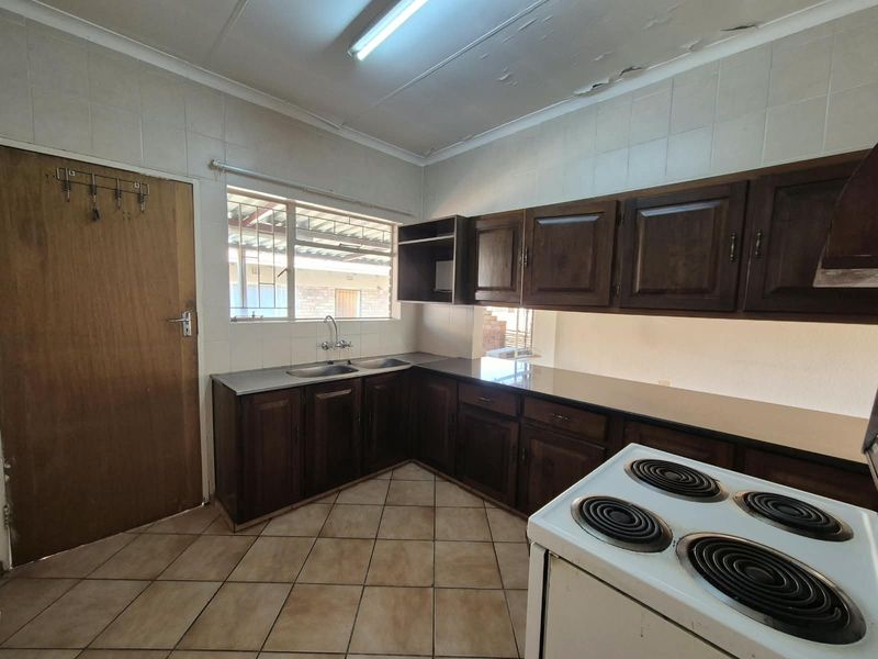 A functional kitchen featuring dark wood cabinetry, tiled flooring, and a double sink, requiring some ceiling maintenance and cosmetic updates.