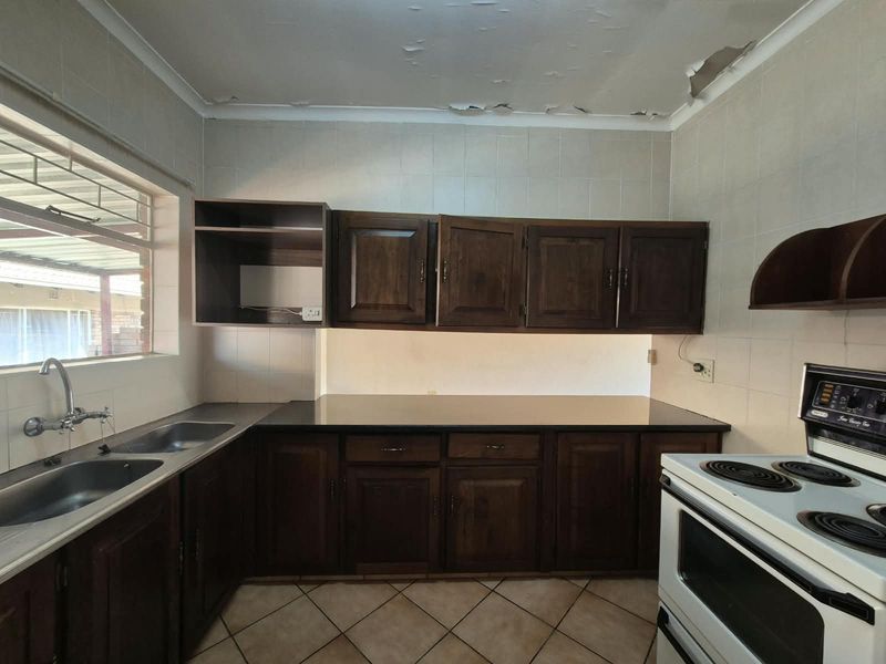 A dated kitchen featuring dark wooden cabinetry, laminate countertops, and a double sink, requiring ceiling repairs and cosmetic updates to modernize the space.