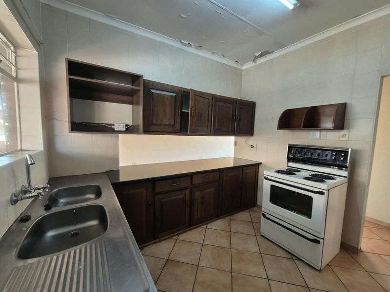 A dated kitchen featuring dark wood cabinetry, a double sink, and a freestanding stove, requiring ceiling repairs and cosmetic updates.