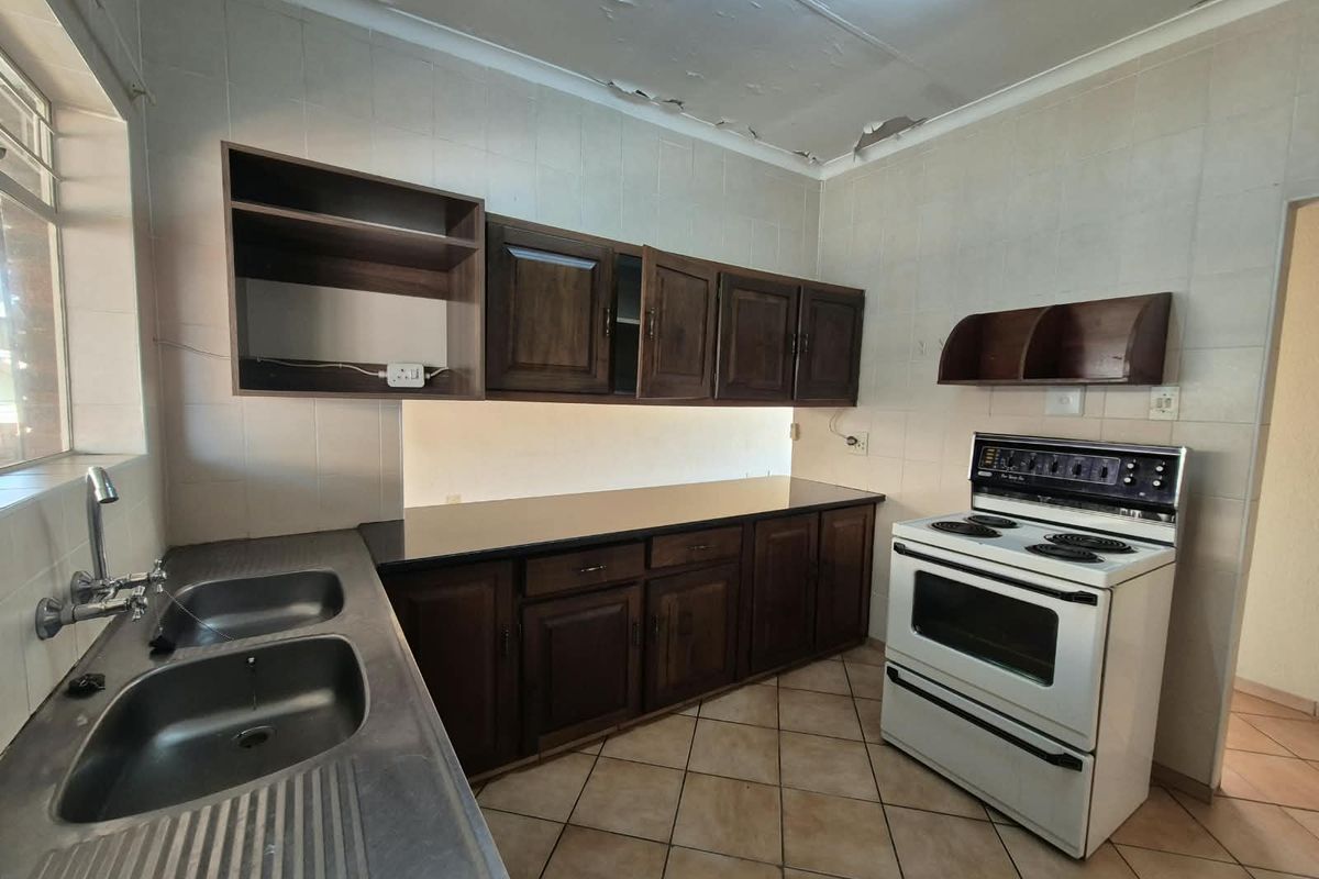 A dated kitchen featuring dark wood cabinetry, a double sink, and a freestanding stove, requiring ceiling repairs and cosmetic updates.
