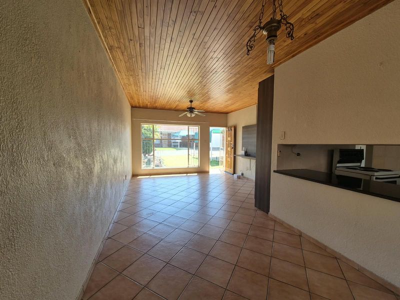 An open-plan living area featuring a warm wooden ceiling, tiled floors, and a breakfast counter, offering a bright and functional space with garden access.