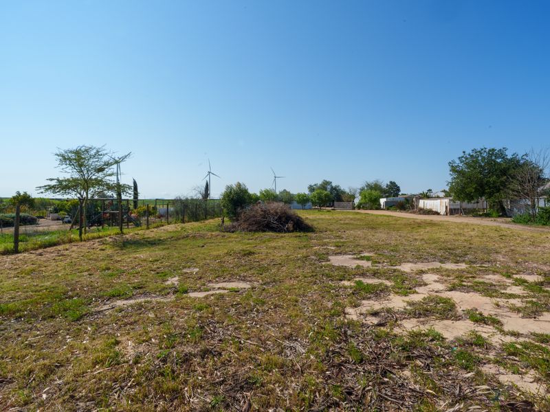 A wide-angle view of a vacant residential plot featuring cleared land, perimeter wire fencing, and surrounding rural landscape.