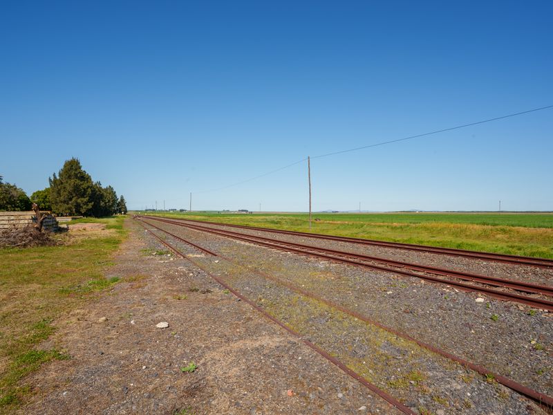A view of railway tracks running through open, undeveloped residential land with surrounding rural landscape and utility infrastructure.