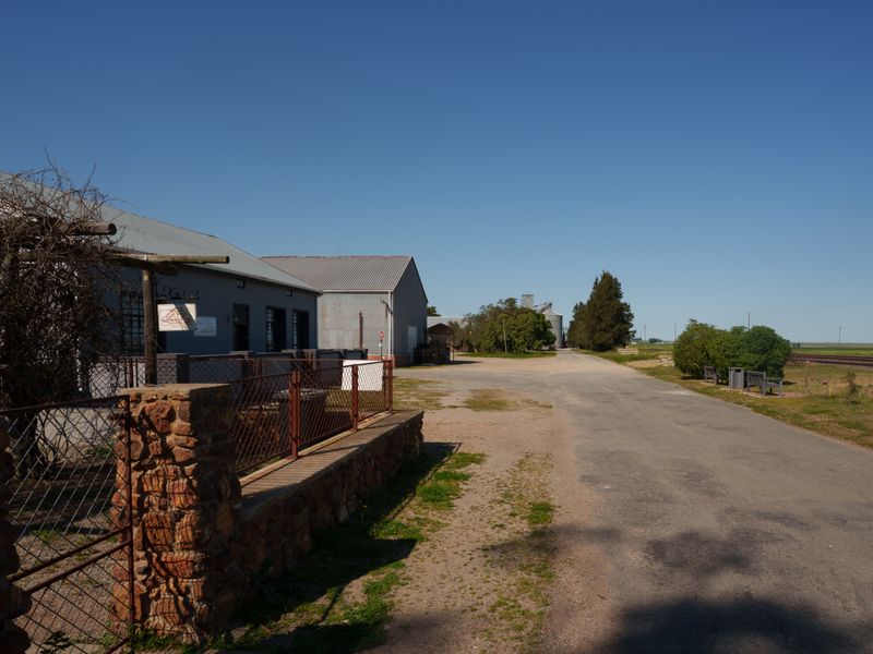 A view of the property frontage featuring a metal-roofed building, stone masonry wall, and adjacent asphalt road in a rural setting.