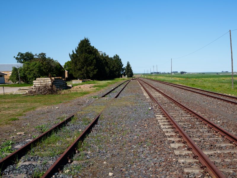 A view of railway tracks running through a rural landscape with adjacent gravel areas and utility infrastructure.