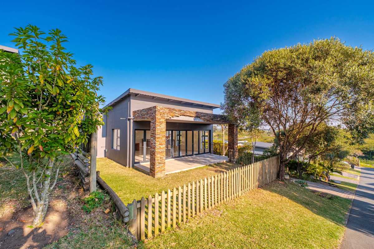 Rear view of a modern home featuring a covered patio with stone-clad pillars, large sliding glass doors, and a landscaped garden with timber fencing.