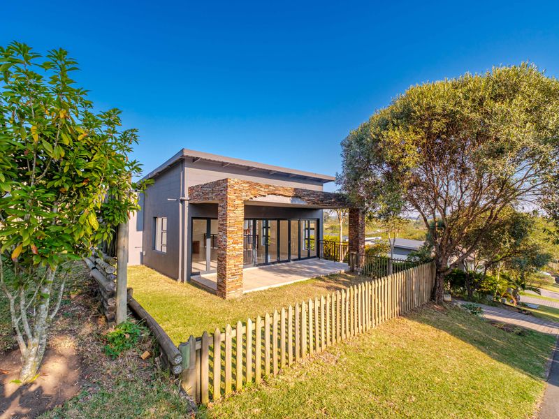Rear view of a modern home featuring a covered patio with stone-clad pillars, large sliding glass doors, and a landscaped garden with timber fencing.