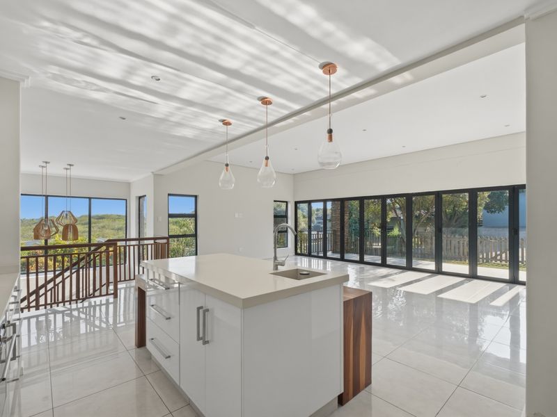 Spacious open-plan kitchen and living area featuring a modern island, sleek cabinetry, large format tiles, and expansive stacking doors leading to the outdoors.