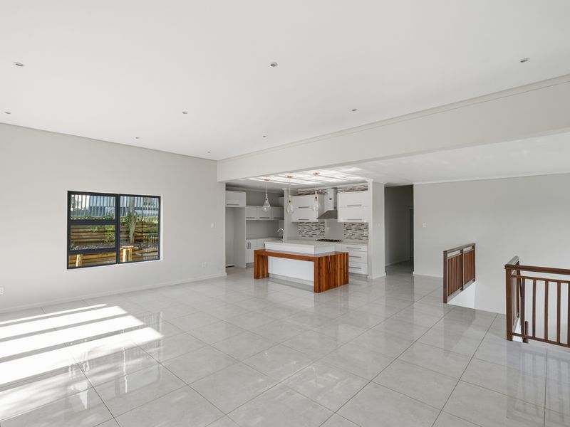 Spacious open-plan living area featuring a modern kitchen with a central island, sleek cabinetry, and tiled flooring, leading to a staircase.