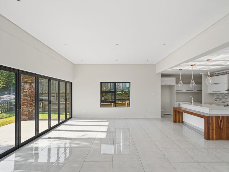 Spacious open-plan living and kitchen area featuring modern cabinetry, stone countertops, large bi-fold doors, and polished tile flooring throughout.
