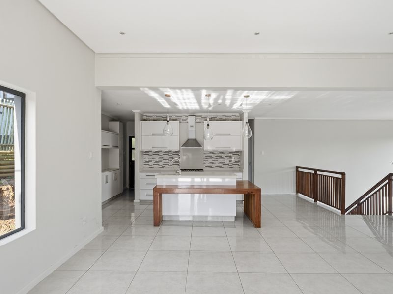 Modern open-plan kitchen and living area featuring sleek white cabinetry, a central island, tiled floors, and a staircase with wooden railings.