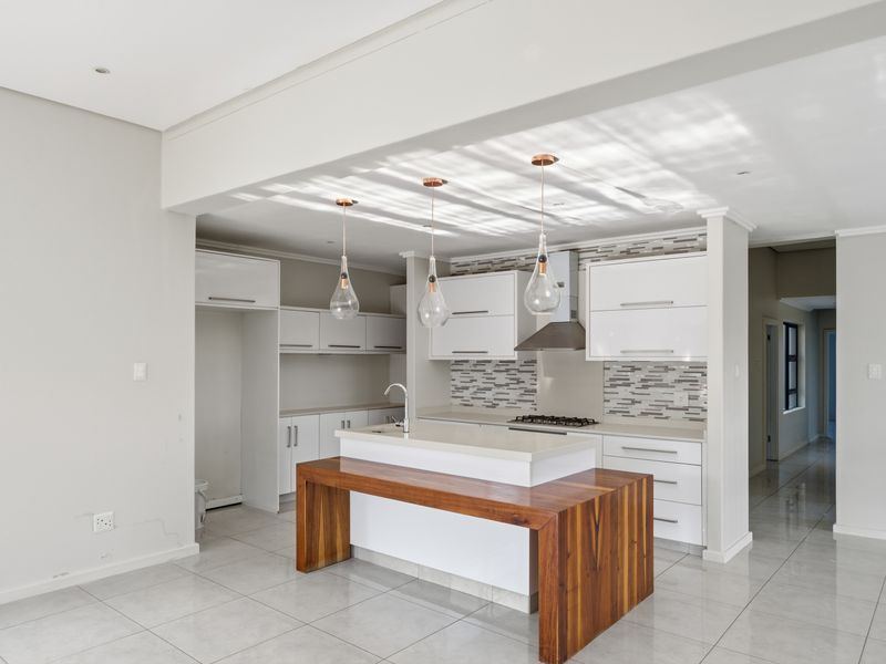 Modern kitchen featuring white cabinetry, a central island with a wooden breakfast bar, stone countertops, gas hob, and stylish pendant lighting.