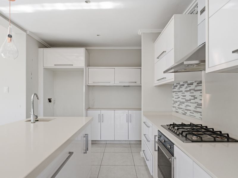 Modern kitchen featuring white high-gloss cabinetry, stone countertops, a gas hob, built-in oven, and a central island with an integrated sink.