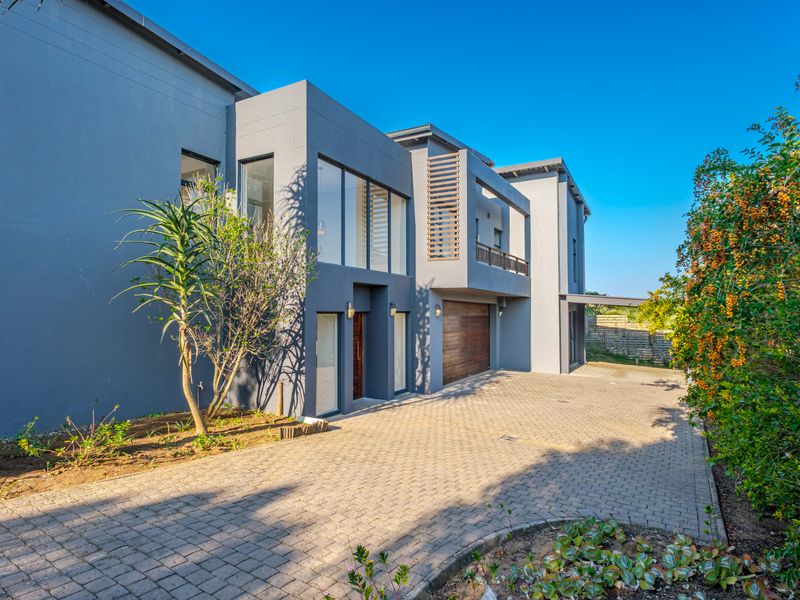 Modern double-story residence featuring a paved driveway, double garage with timber door, and a contemporary facade with large windows and a balcony.