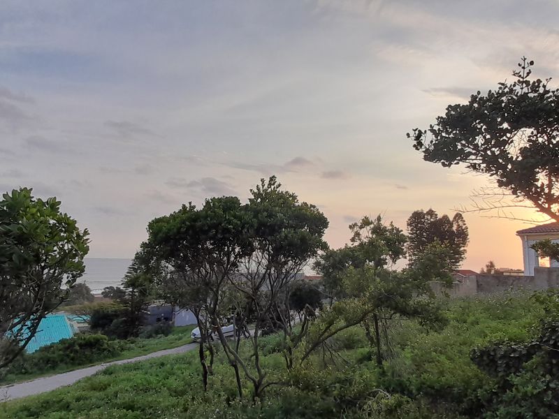 A scenic view of the coastal landscape at sunset, showcasing natural vegetation and the surrounding environment of the vacant residential land.