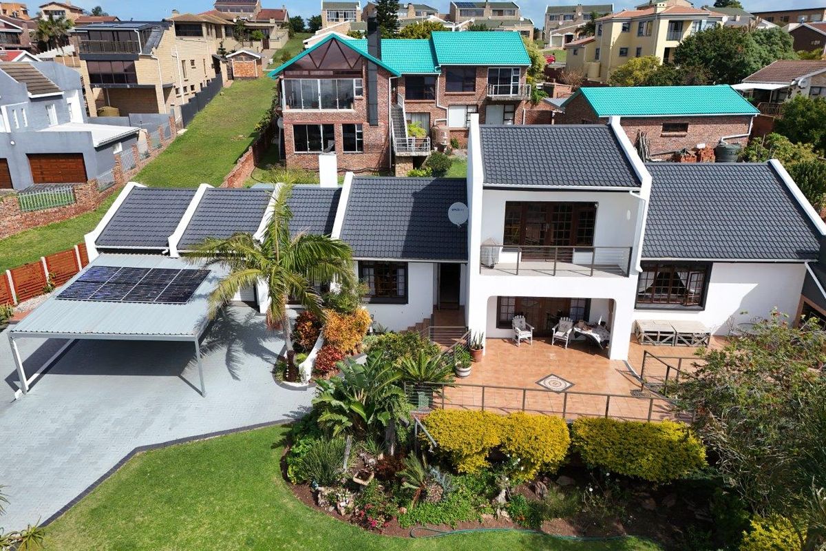 Aerial view of a well-maintained residential property featuring a tiled roof, solar panels, a paved carport, and a spacious patio overlooking a landscaped garden.