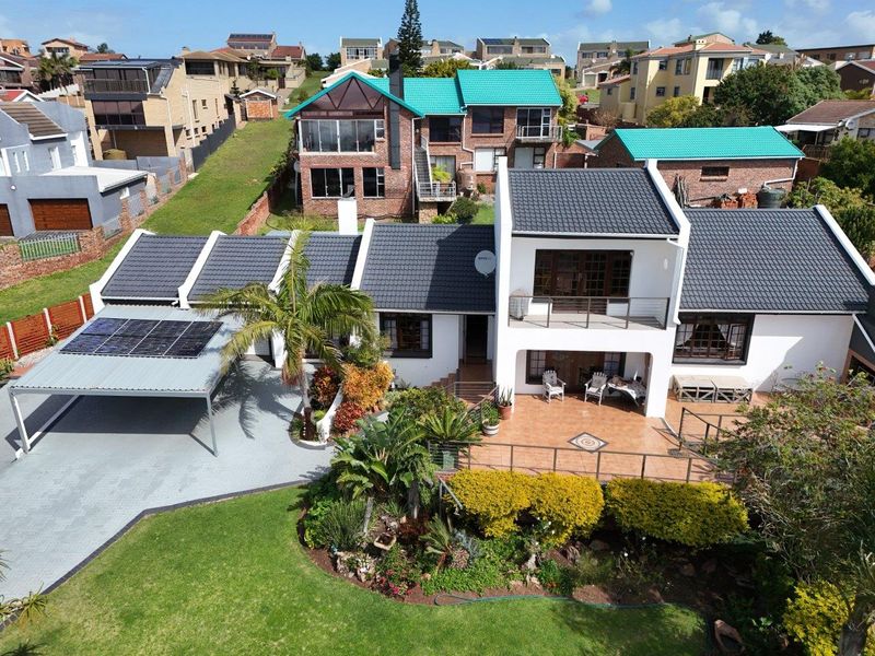 Aerial view of a well-maintained residential property featuring a tiled roof, solar panels, a paved carport, and a spacious patio overlooking a landscaped garden.