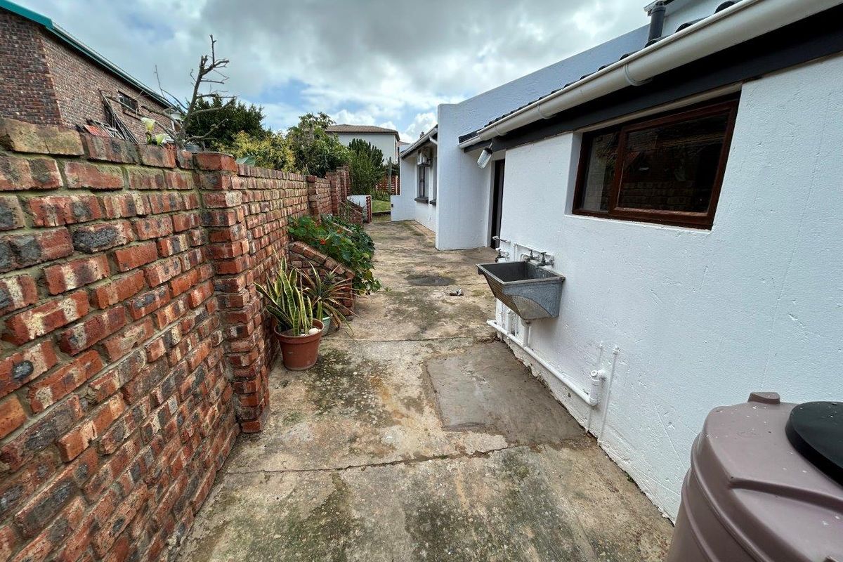Rear exterior area featuring a brick boundary wall, concrete paving, and a wall-mounted utility sink along the side of the house.