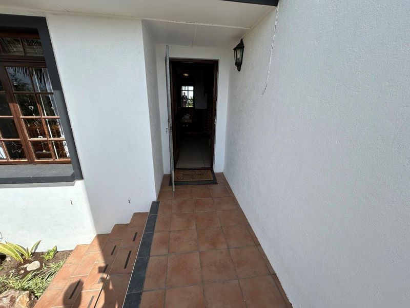 A covered entrance porch featuring tiled flooring, exterior lighting, and steps leading to the main doorway.