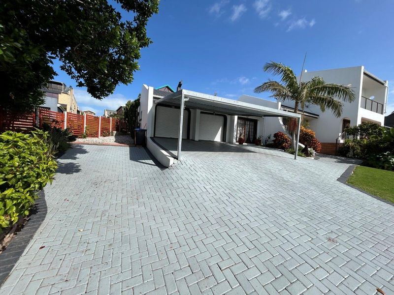 Front exterior view featuring a paved driveway, double garage, and a covered carport area with established landscaping.