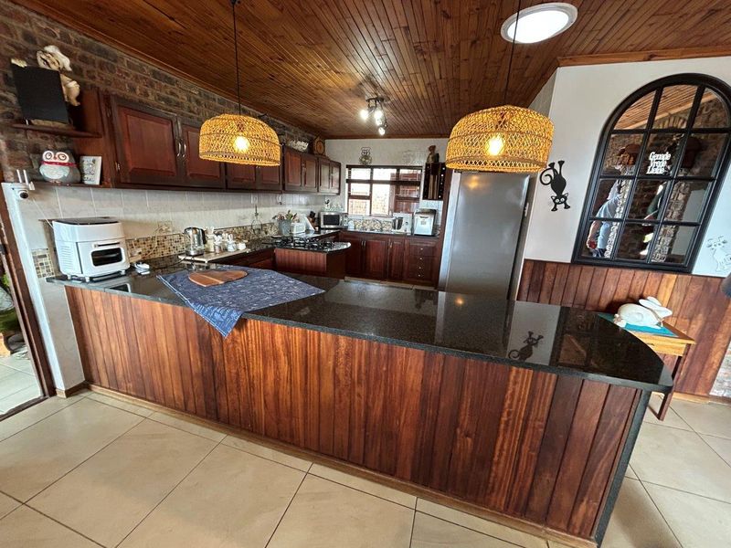 A rustic-style kitchen featuring dark wood cabinetry, granite countertops, a breakfast bar, and a distinctive timber-clad ceiling with exposed brick accents.