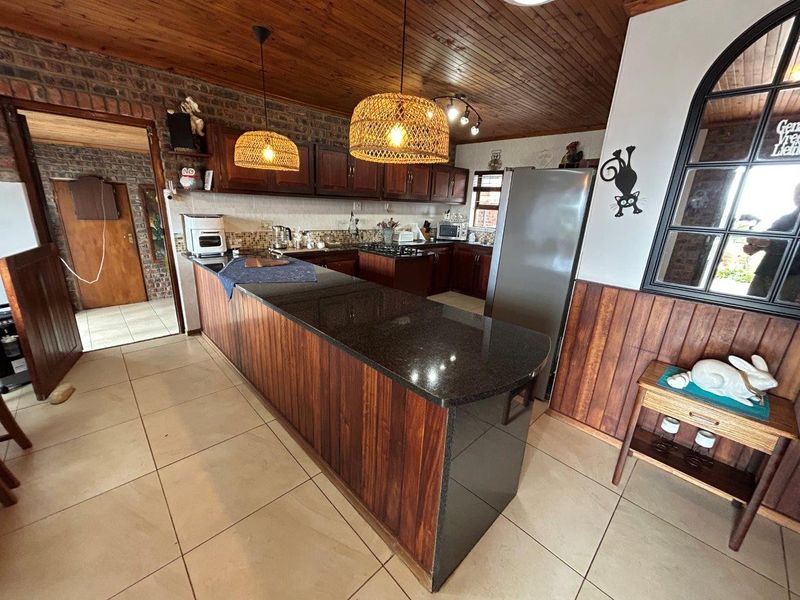 A spacious kitchen featuring dark wooden cabinetry, granite countertops, a gas hob, and a distinctive timber-paneled ceiling with exposed brick accents.