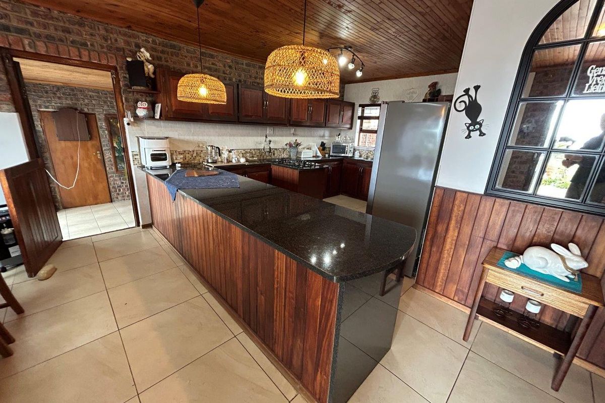 A spacious kitchen featuring dark wooden cabinetry, granite countertops, a gas hob, and a distinctive timber-paneled ceiling with exposed brick accents.