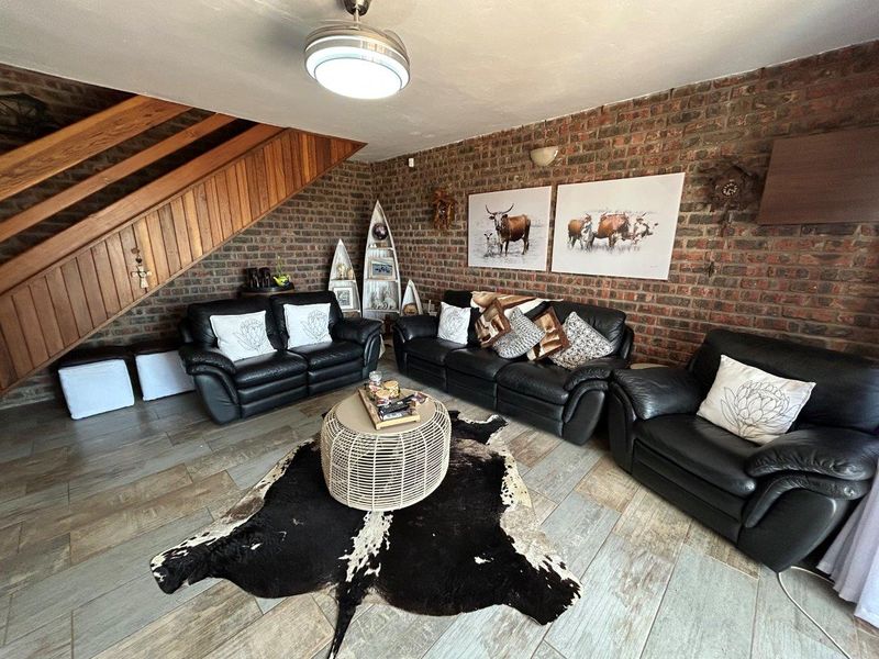 A living room featuring exposed brick walls, tiled flooring, and a wooden staircase, offering a rustic aesthetic with potential for modern updates.