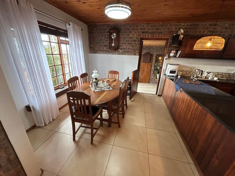 Open-plan kitchen and dining area featuring exposed brick walls, timber ceiling, tiled flooring, and fitted cabinetry with granite countertops.