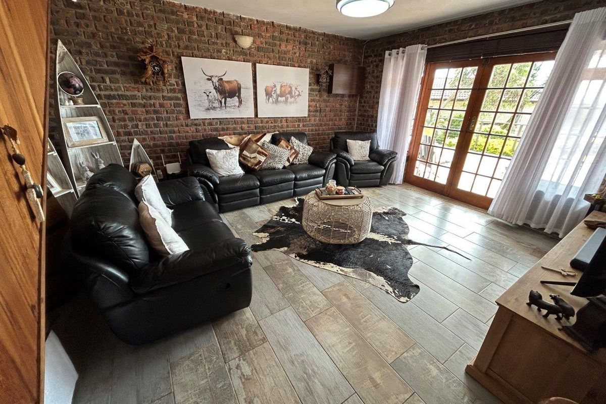 A cozy living room featuring an exposed brick feature wall, wood-look tiled flooring, and double french doors providing access to the outdoor area.