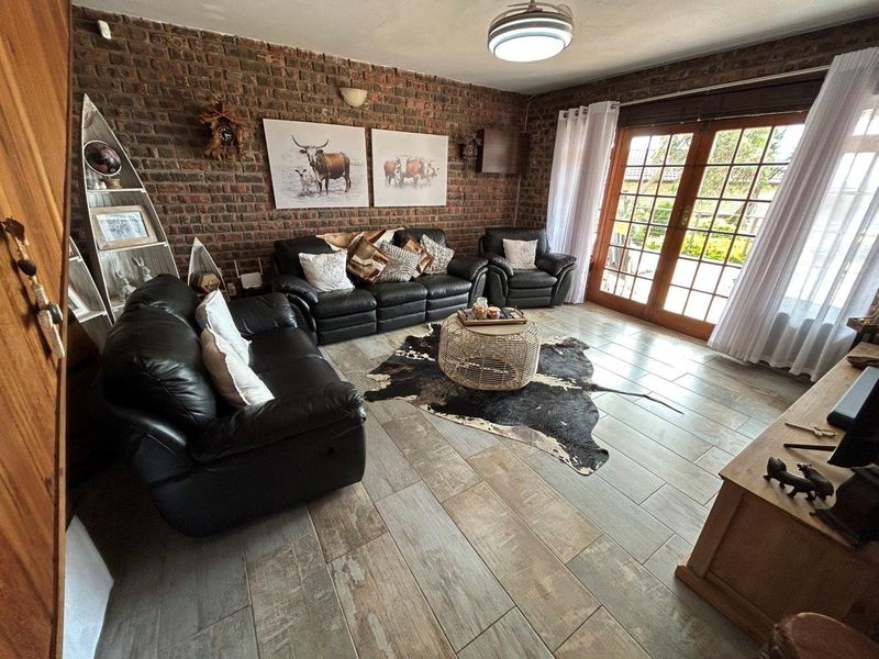 A cozy living room featuring an exposed brick feature wall, wood-look tiled flooring, and double french doors providing access to the outdoor area.