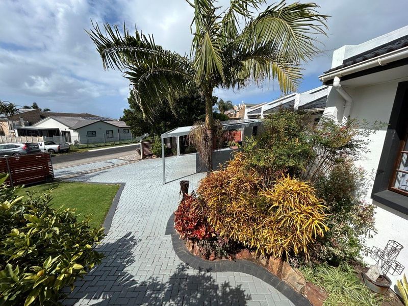 Front exterior view featuring a paved driveway, landscaped garden beds, and a carport structure.