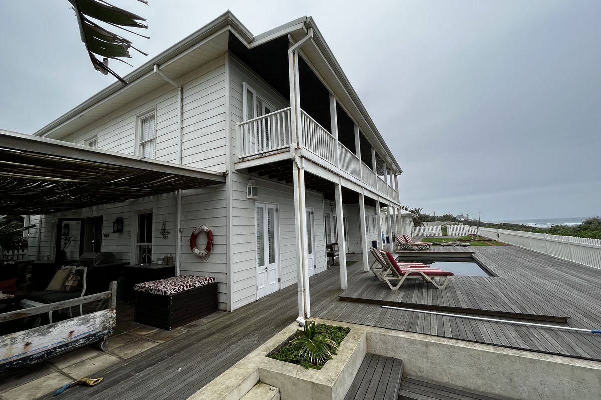 Rear exterior view featuring a spacious timber deck, swimming pool, covered patio area, and a two-story building with balcony access.