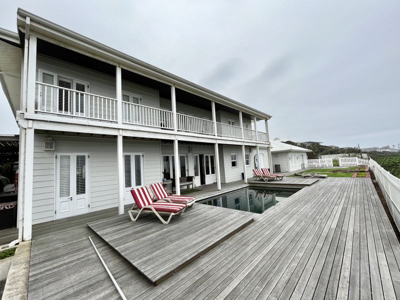 Spacious rear exterior featuring a large timber deck, swimming pool, and a two-story residence with covered veranda and balcony.