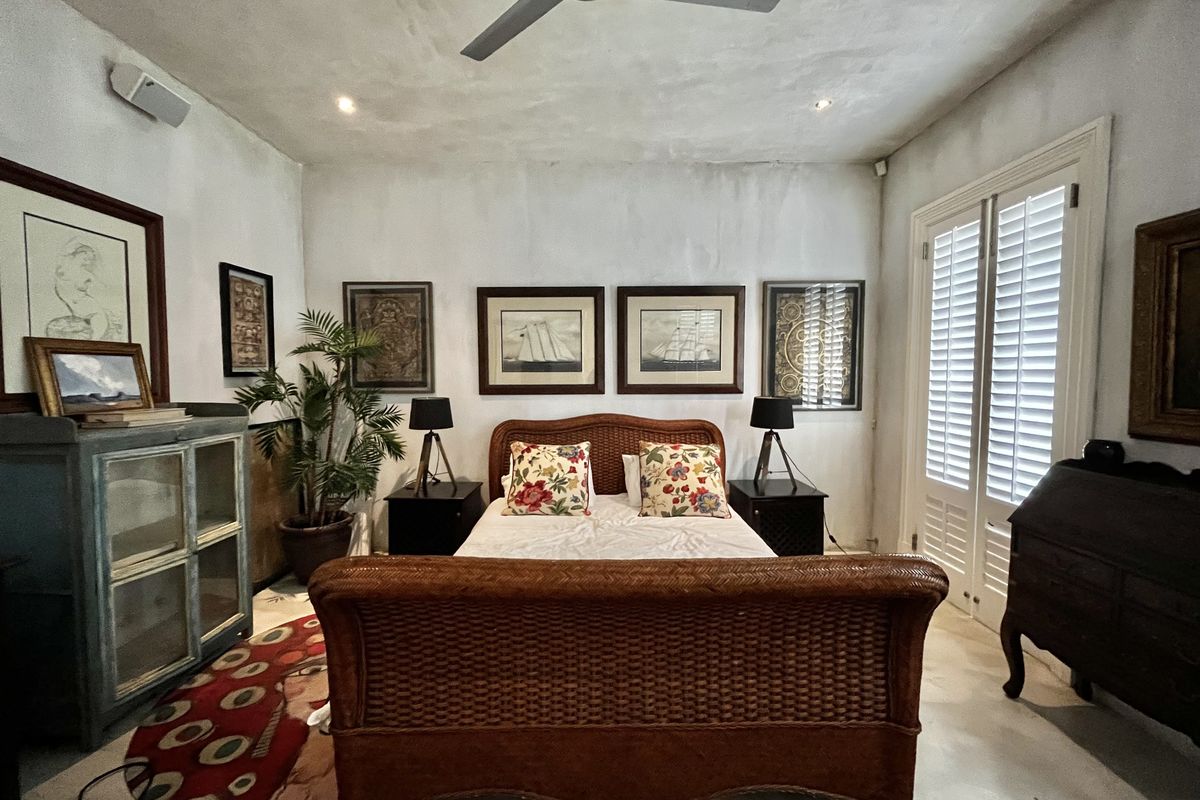 A bedroom featuring a ceiling fan, recessed lighting, and plantation shutters. The walls show signs of uneven texture and staining.