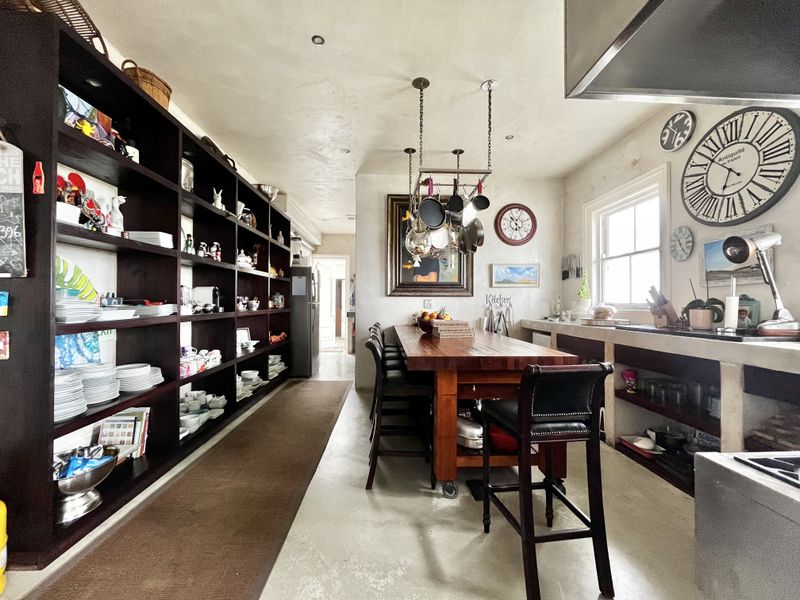 A spacious kitchen featuring extensive built-in shelving, a central wooden island with a hanging pot rack, and durable concrete countertops and flooring.
