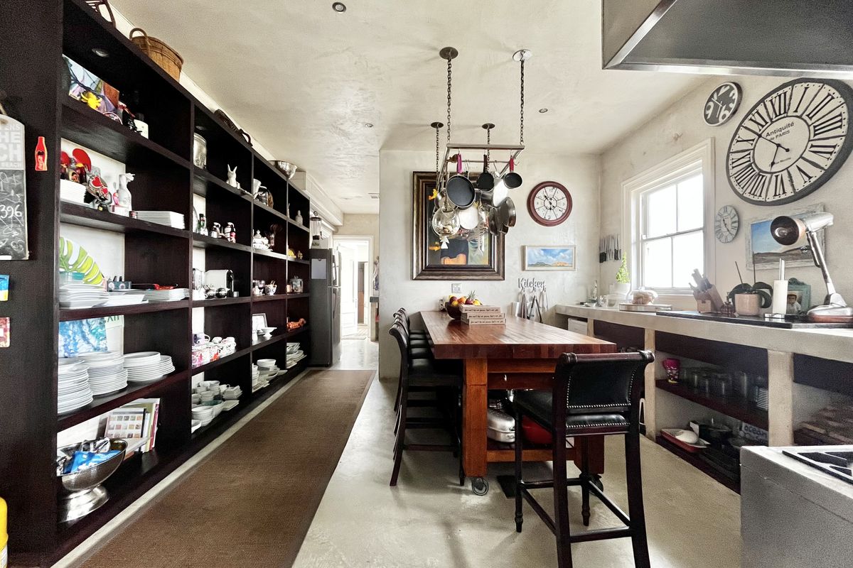 A spacious kitchen featuring extensive built-in shelving, a central wooden island with a hanging pot rack, and durable concrete countertops and flooring.