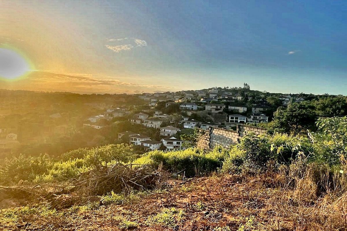 A scenic elevated view overlooking a residential neighborhood at sunset, featuring natural terrain and a partial retaining wall structure.