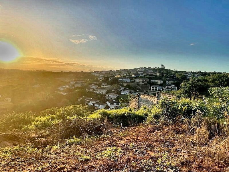 A scenic elevated view overlooking a residential neighborhood at sunset, featuring natural terrain and a partial retaining wall structure.