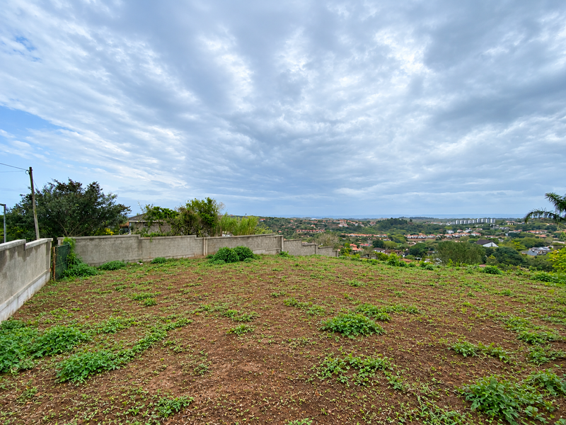 A vacant residential plot featuring a perimeter boundary wall and elevated views over the surrounding neighborhood and landscape.