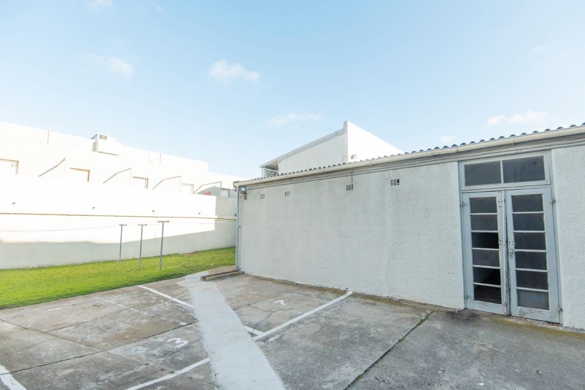 Rear exterior view of the apartment featuring a concrete paved area, small lawn, and access via glass-paned french doors.
