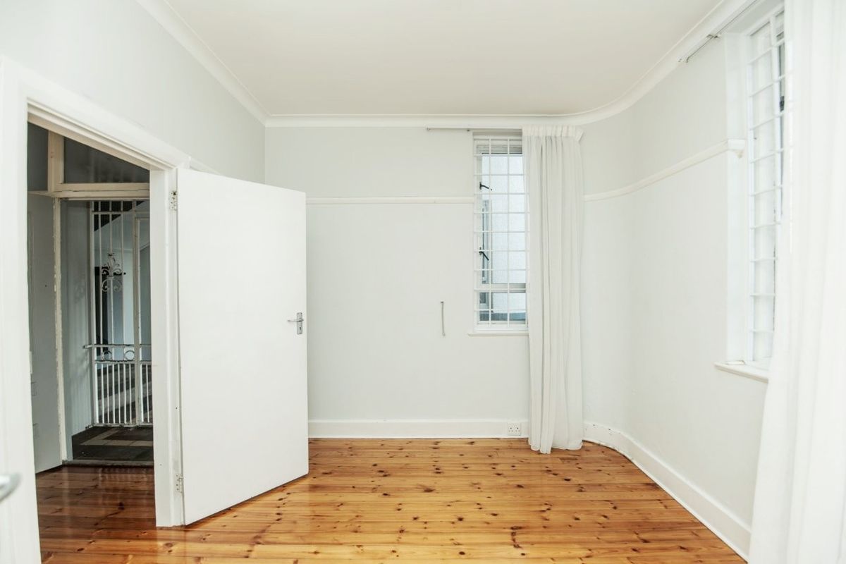 A bright, empty bedroom featuring polished timber flooring, coved cornicing, and windows fitted with security bars.