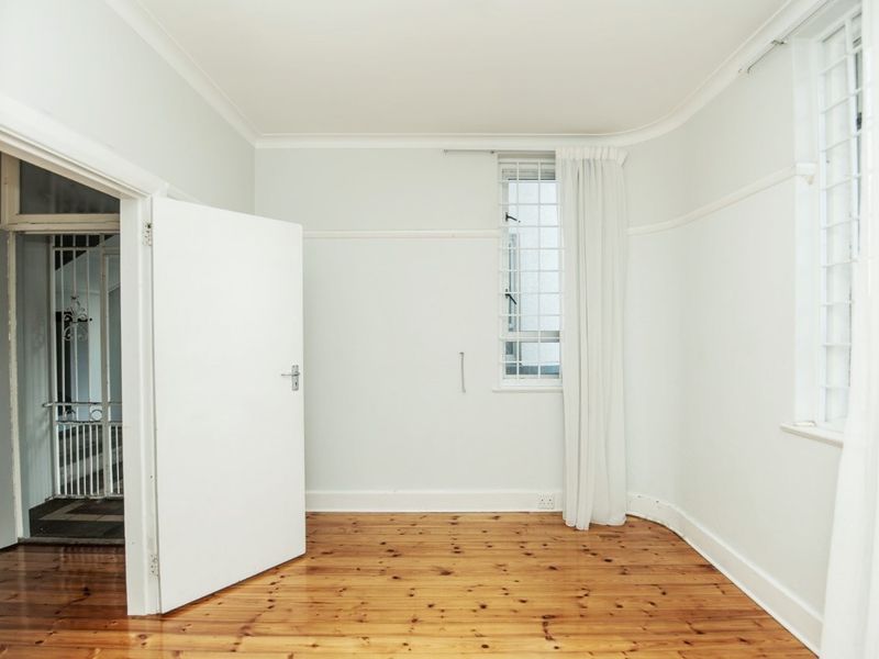 A bright, empty bedroom featuring polished timber flooring, coved cornicing, and windows fitted with security bars.