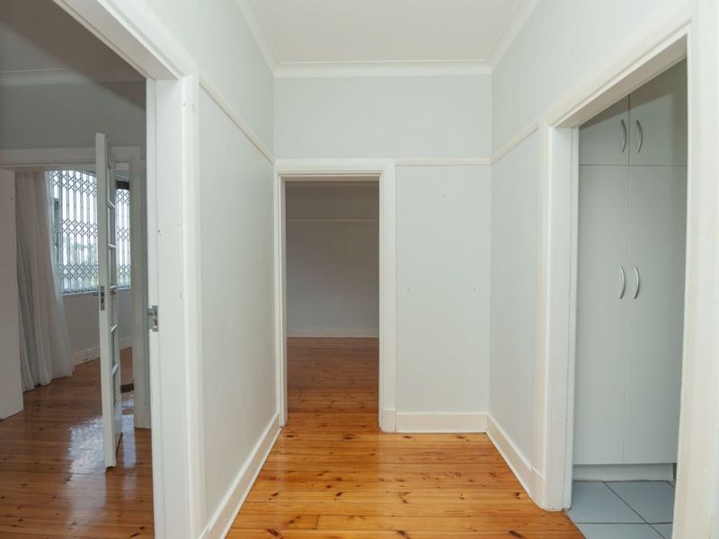 A bright, empty hallway featuring polished timber flooring, built-in storage cupboards, and classic architectural detailing connecting multiple rooms.