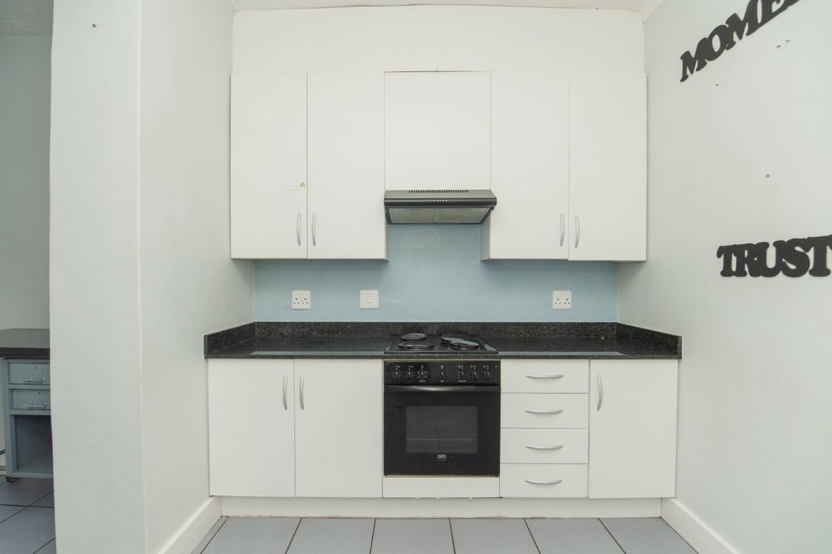 A compact kitchen featuring white built-in cabinetry, dark granite countertops, an integrated oven and stove, and a light blue backsplash.