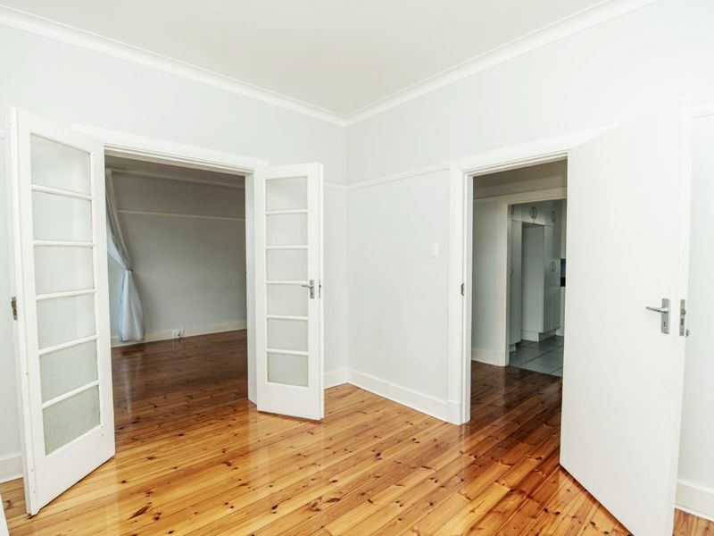 A bright, empty hallway featuring polished timber flooring, classic picture rails, and elegant french doors connecting to adjacent living spaces.
