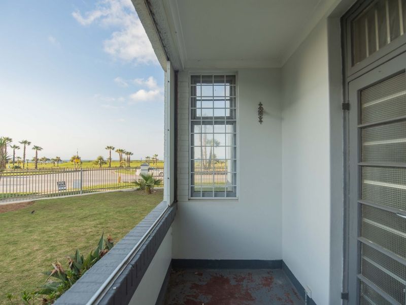A covered balcony area featuring security bars on the window and direct access to the exterior, offering views of the surrounding garden and street.