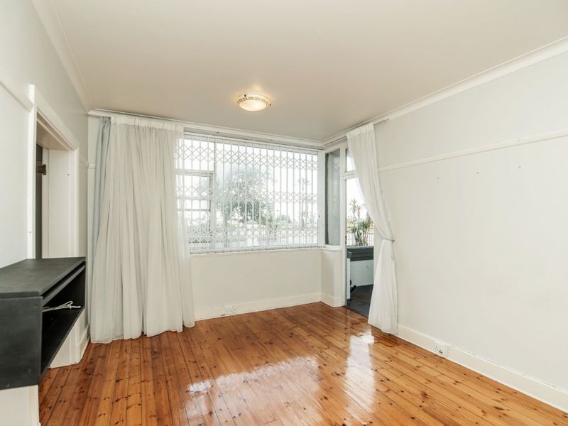 A bright, empty living room featuring polished timber flooring, a security gate on the window, and direct access to an outdoor area.